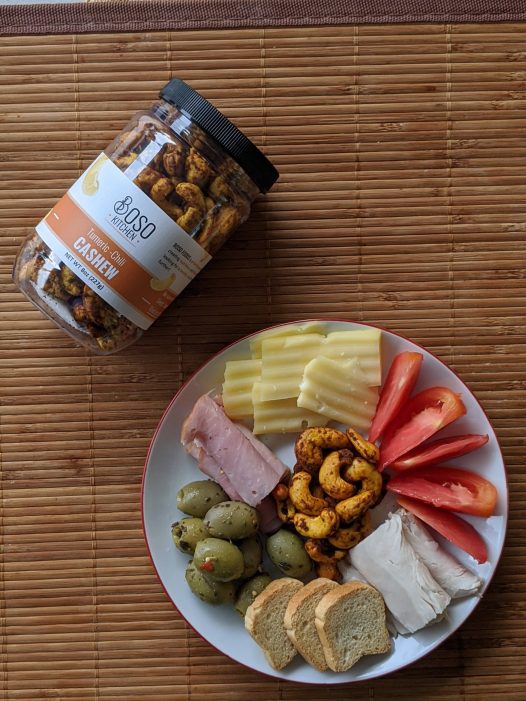A ohoto of turmeric cashews displayed in a mii cheese plate that includes tomatoes, olives, turkey and cheese.