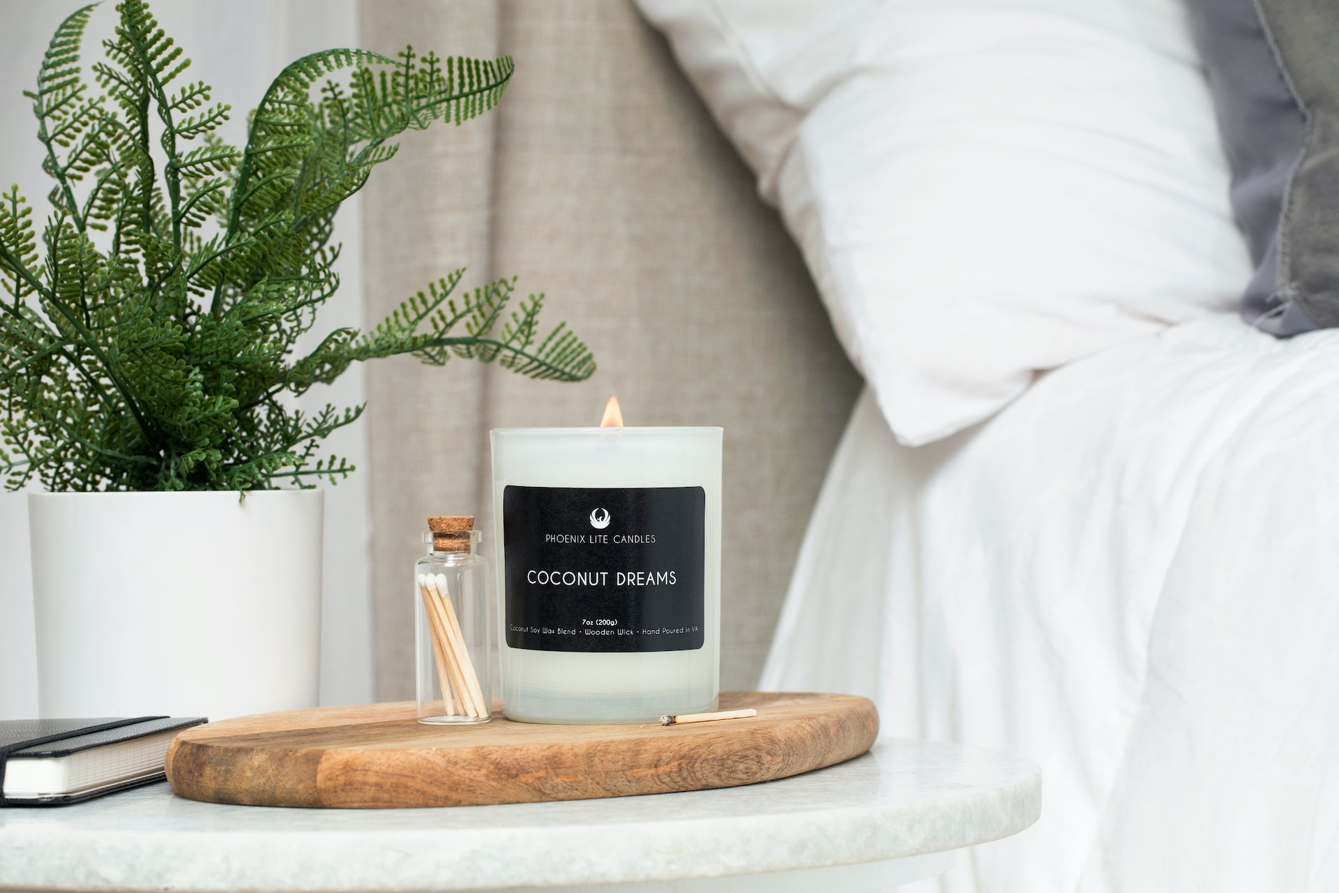 A photo of a lit seven ounce candle in a white jar labeled coconut dreams