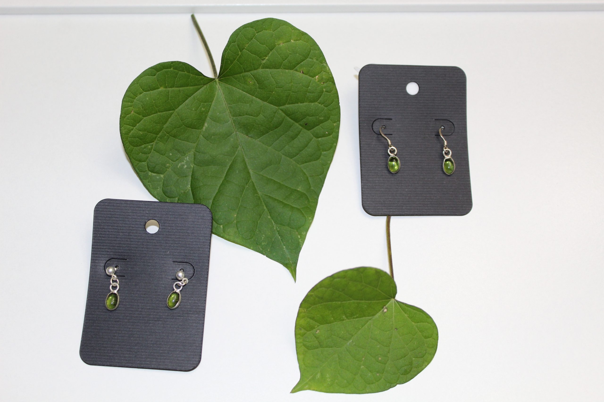 Two pairs of simple silver and green dangle earrings on a white background with morning glory leaves.