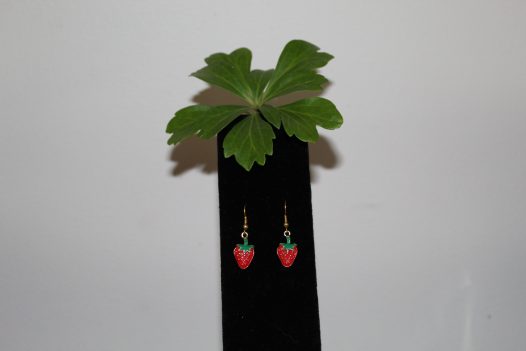 Strawberry dangle earrings on a black stand with a sprig of Japanese pachysandra.