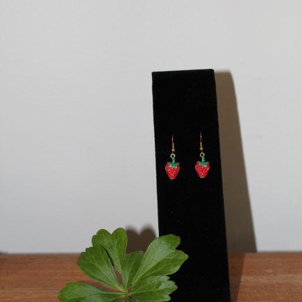 Strawberry dangle earrings on a black stand with a sprig of Japanese pachysandra.