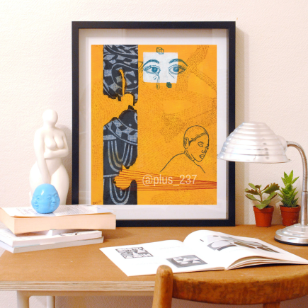 Art print of Ancestors Are Watching, a yellow abstract art print with Ndop fabric, in a black frame, sitting on top of a wooden table with knickknacks, lamp and books