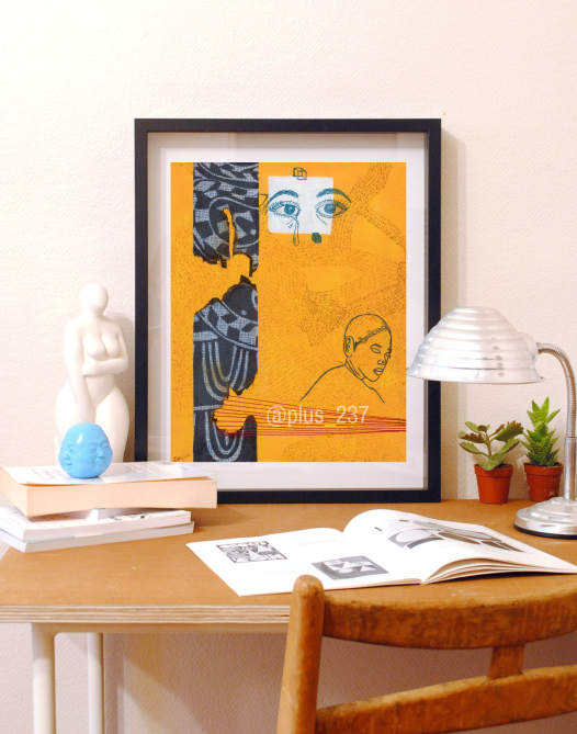 Art print of Ancestors Are Watching, a yellow abstract art print with Ndop fabric, in a black frame, sitting on top of a wooden table with knickknacks, lamp and books