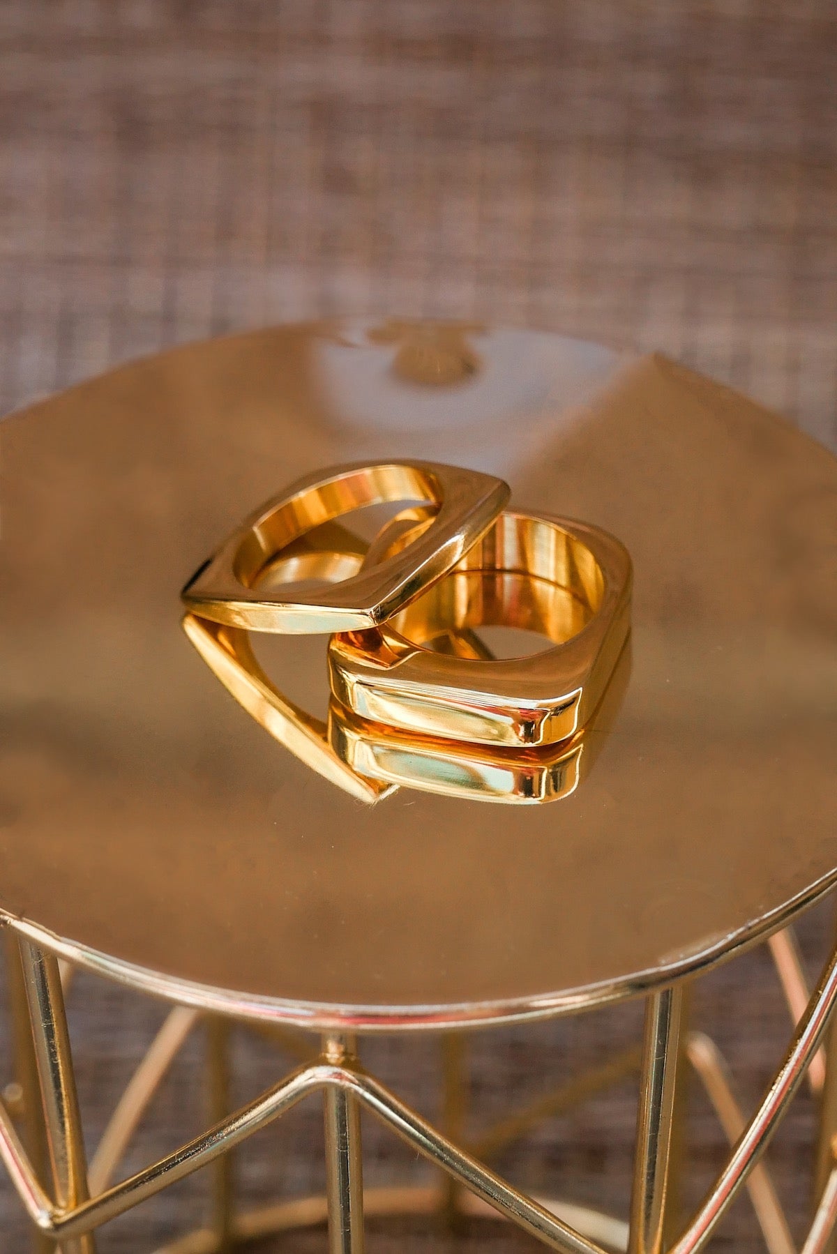 Two square gold out of the box rings on a gold table