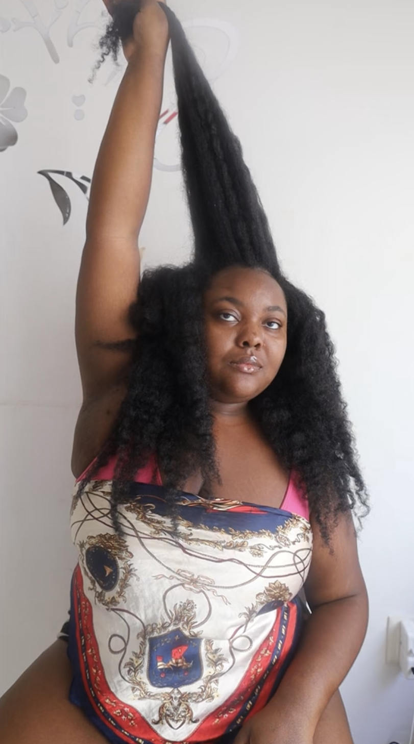 The vendor of the Growth Training Guide sitting in a chair, and holding a portion of her hair up toward the sky to show its length.