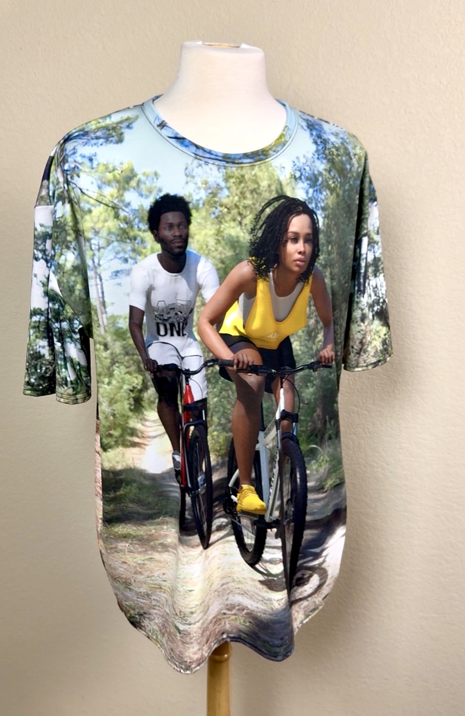 An all over print t-shirt with a picture of a black couple riding bicycles on a wooded path.